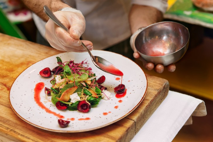 Professional chef is pouring red sauce on vegetable and berry appetizer, toned image