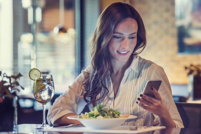 woman using phone while eating a salad