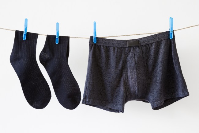 Man's clean black socks and boxer shorts. Underwear drying on laundry rope at white wall. Dry cleaning. Regular washing. Daily routine. Clothes care.