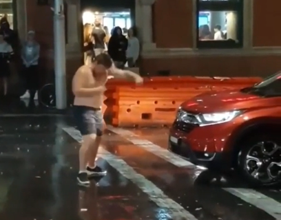 Shirtless man in Australia tries to fight a car in the middle of the street during pouring rain in front of KFC restaurant. 