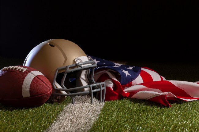 Low angle view of a football, helmet and American flag on a grass field with stripe and dark background