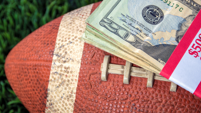 A football lays on the field with money on top.