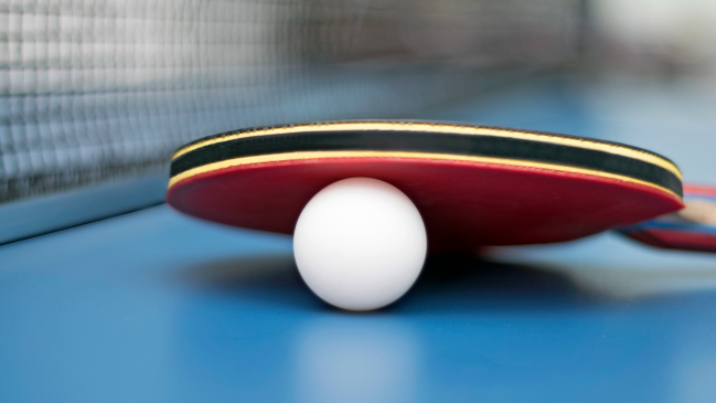 A table tennis paddle sits on a ping pong ball.