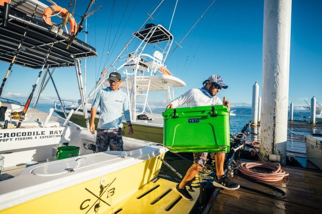 Fisherman lifting a YETI canopy green color Tundra cooler on a sport fishing boat