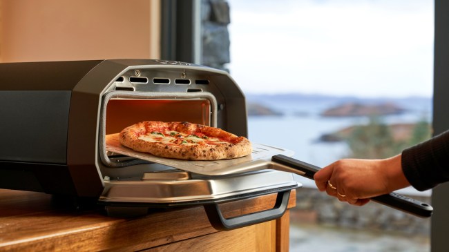 The Ooni Volt 12 electric pizza oven in a kitchen setting, with a pizza coming out of the oven