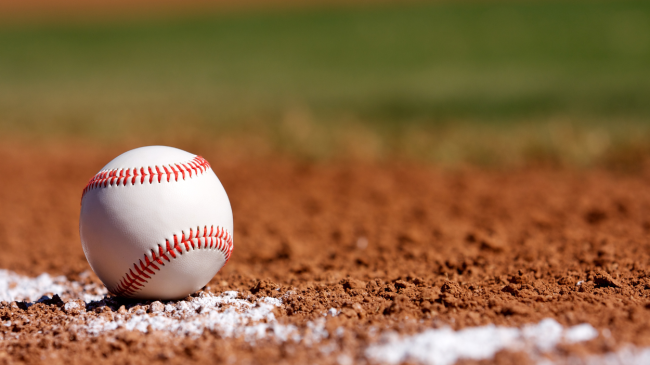 A baseball rests on the clay of a baseball diamond.