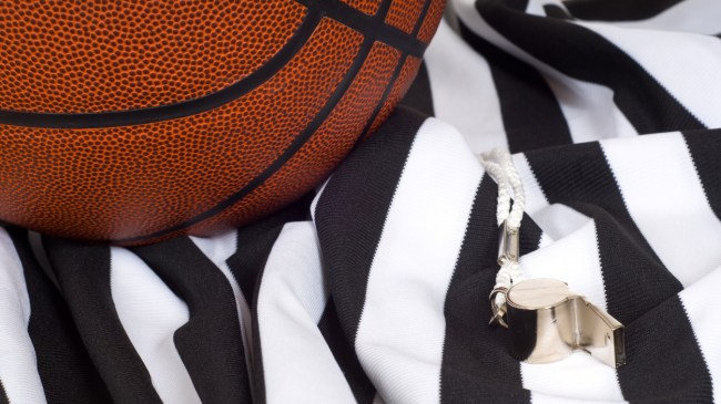 A basketball lays by a referee jersey and whistle.