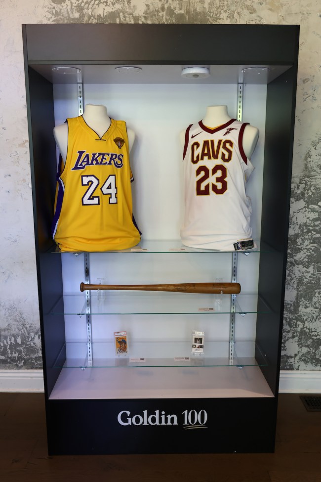 Kobe Bryant and Lebron James jerseys, a Jackie Robinson baseball bat, and sports cards in a glass case