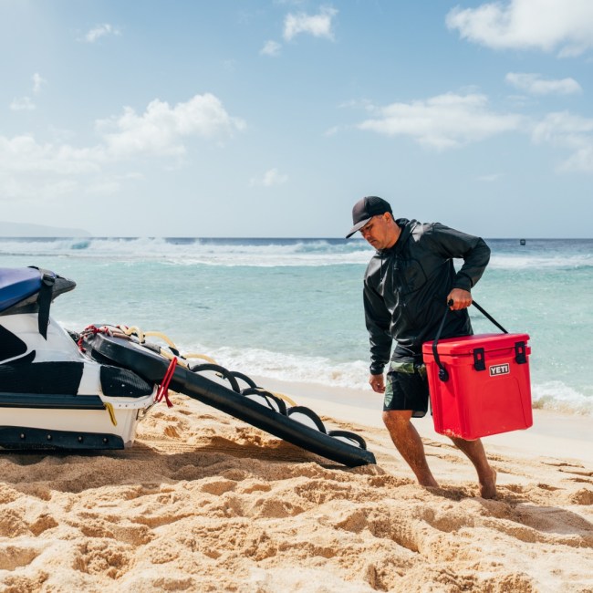 Lifeguard carrying a rescue red color YETI cooler on a beach