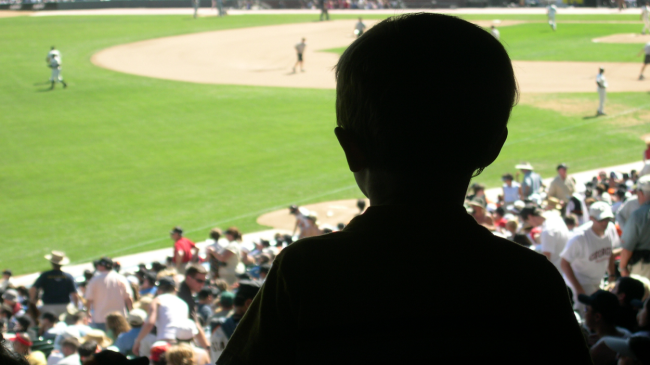 A small fan watches a baseball game from the stands.