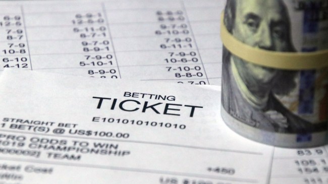 A roll of money sits on top of a betting ticket.