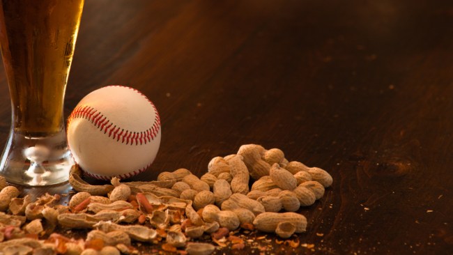 A baseball sits atop a bar beside a beer and roasted peanuts.