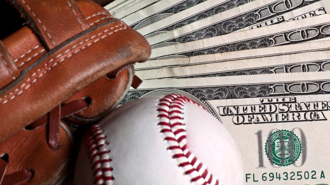 A baseball and glove sit on a stack of $100 bills.