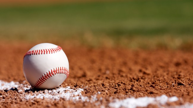 A baseball rests on the third base line on the infield.