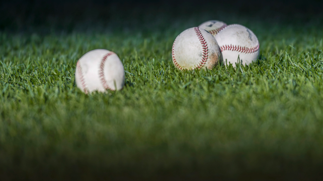 Four baseballs lie in the outfield grass.