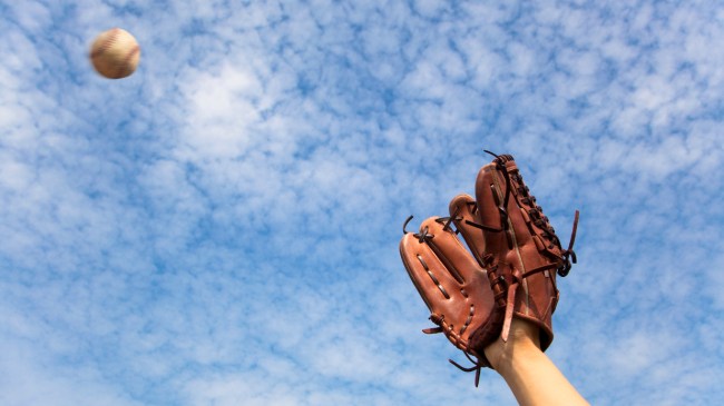 A player reaches out with his glove to catch a baseball.