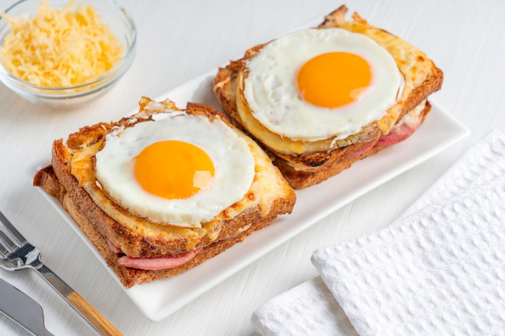 Two hot baked French sandwiches named Croque Madame with ham, cheese and bread slices topped with fried edd served on plate