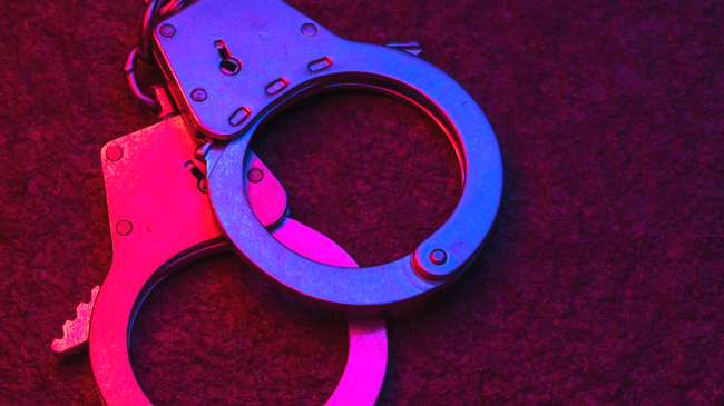 Handcuffs on dark background illuminated by flashing lights of police car