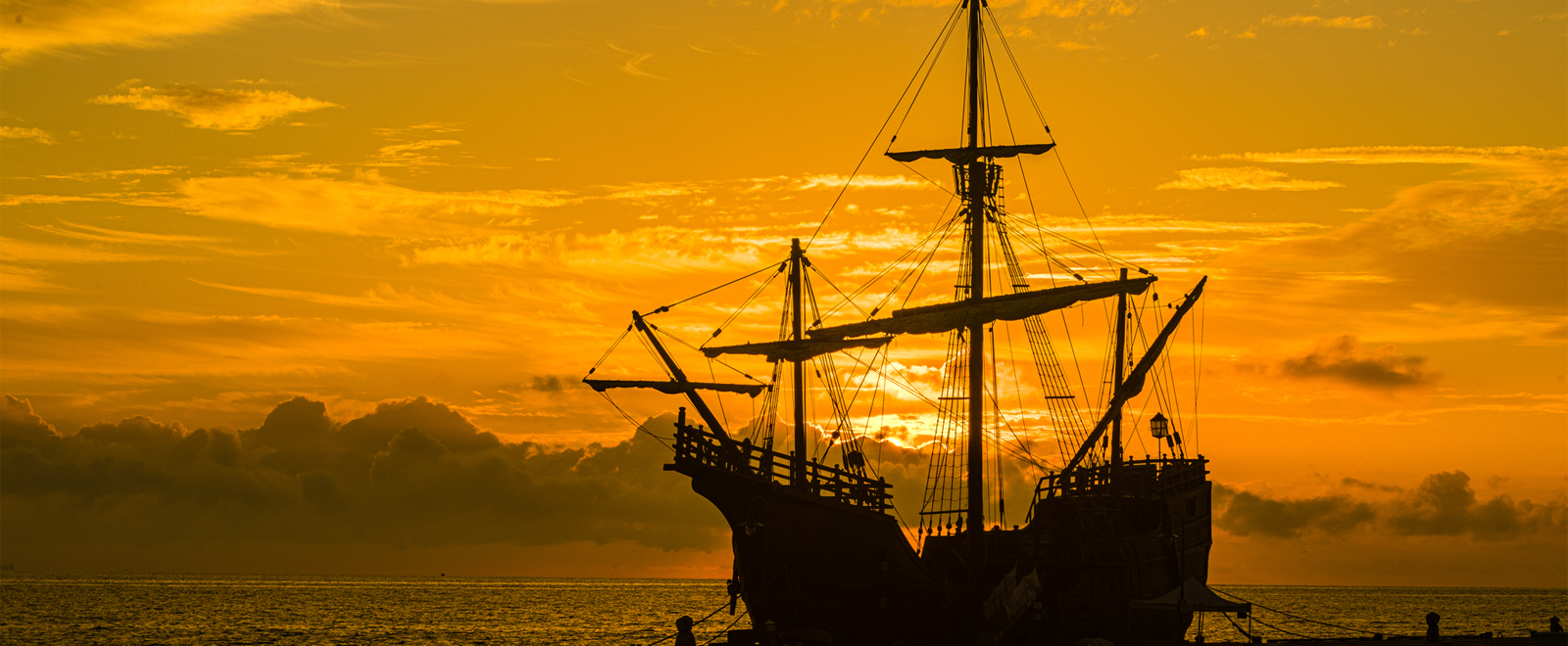 spanish galleon at sunrise with orange sky behind the ship