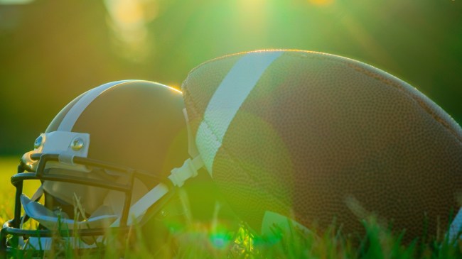 A football rests against a helmet on the grass.