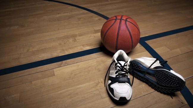 A basketball rests next to a pair of sneakers on the court.