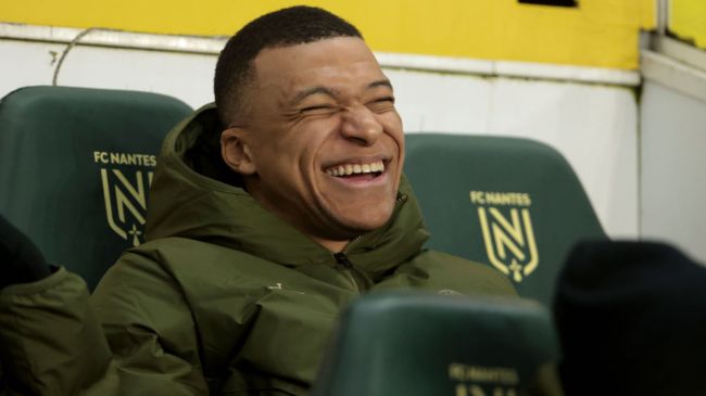 kylian mbappe laughing while sitting on the bench