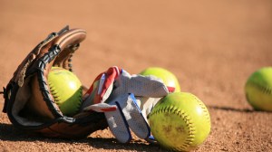 Softballs sit next to a mitt on the infield clay.