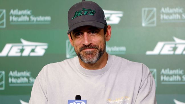 aaron rodgers speaking at a podium wearing a jets hat