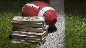 A stack of money on the field next to a football.