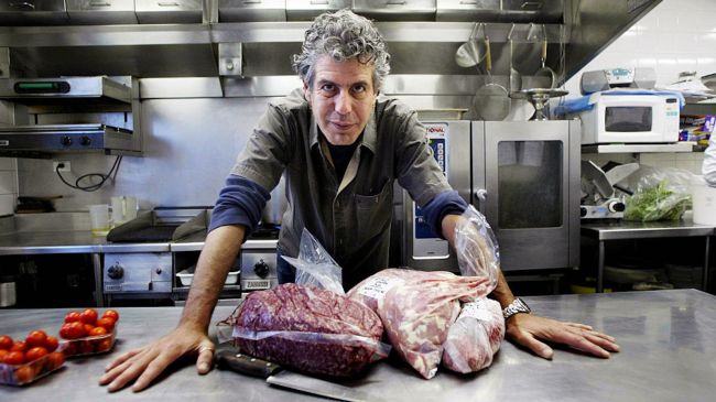 anthony bourdain with meat in a kitchen
