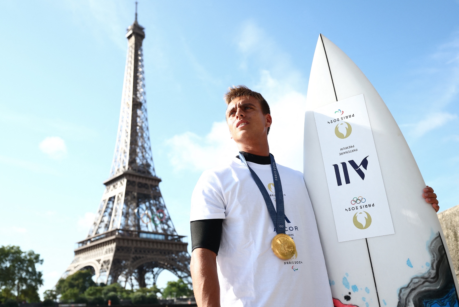 Gold medalist Kauli Vaast posing with surfboard in front of Eiffel Tower