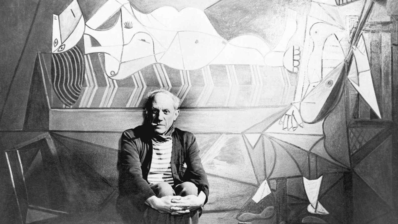 Pablo Picasso sitting in front of a painting