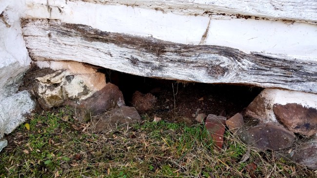 Crawlspace hole underneath white wood and stone house