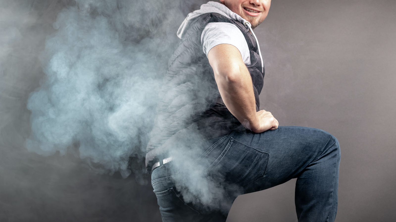 Man lift the leg and fart in front of grey background