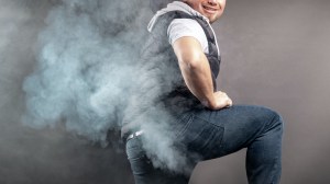 Man lift the leg and fart in front of grey background