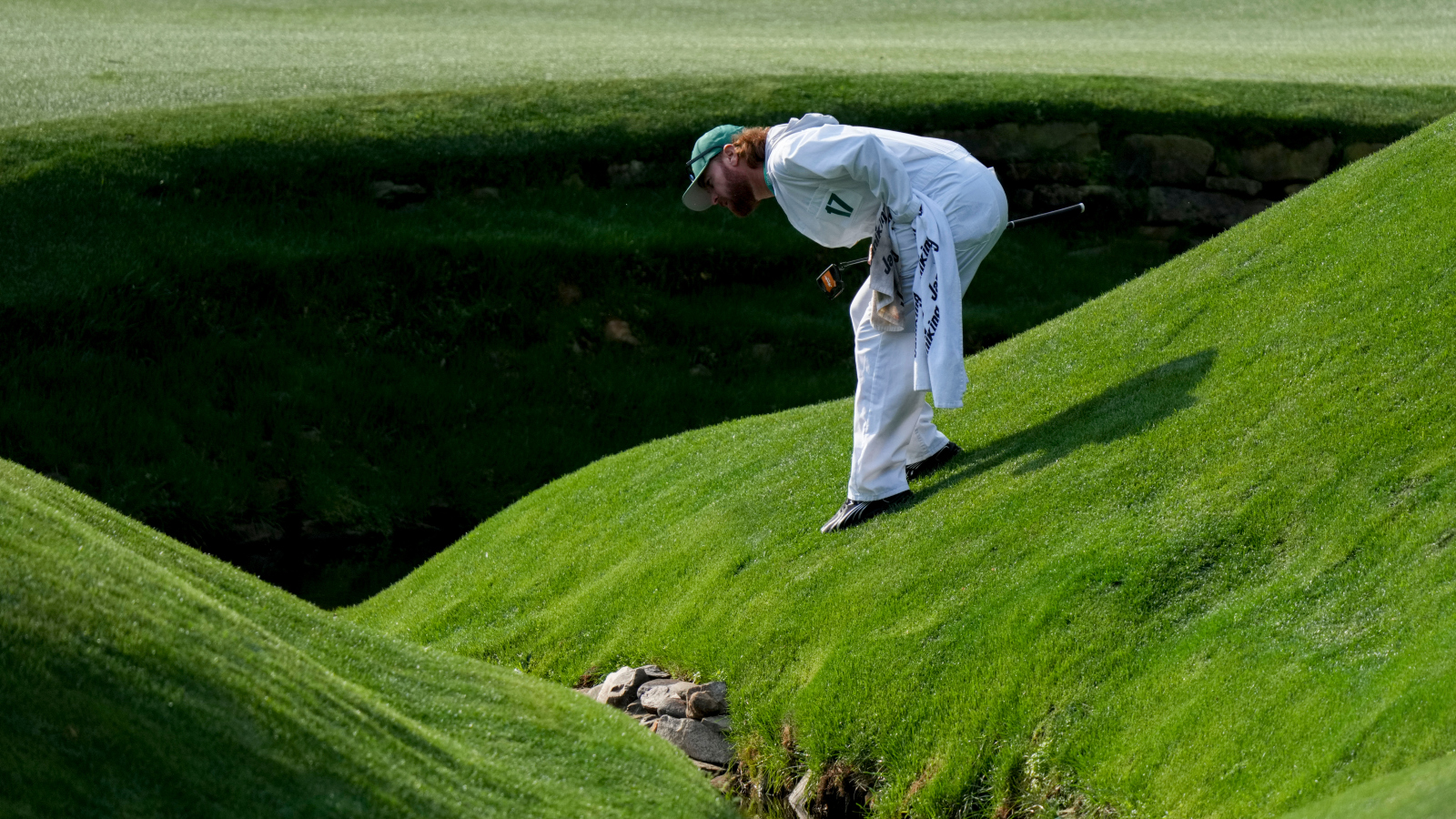 caddie looking for ball in the water at Amen Corner