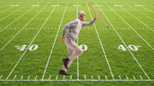 old man running on a football field holding a cane