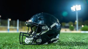 American football helmet on grass under stadium lights at night, evoking competition, teamwork and dedication on the empty gridiron before kickoff