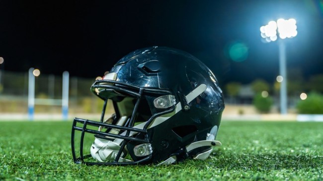 American football helmet on grass under stadium lights at night, evoking competition, teamwork and dedication on the empty gridiron before kickoff