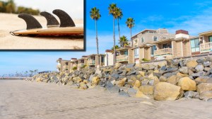 Surfboard laying on the sand in Oceanside, California next to rocks protecting the shore
