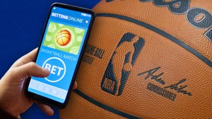 Person using betting app next to NBA basketball